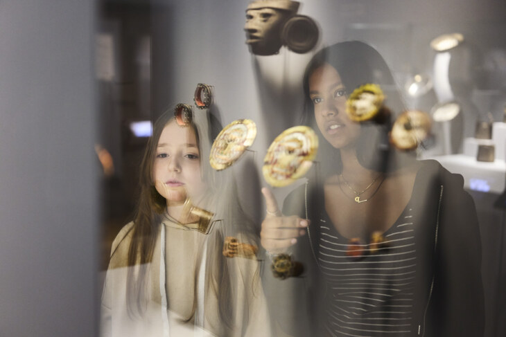 Zwei Mädchen schauen in eine Vitrine, die mit Ohrschmuck aus der neuen Welt ausgestellt ist.