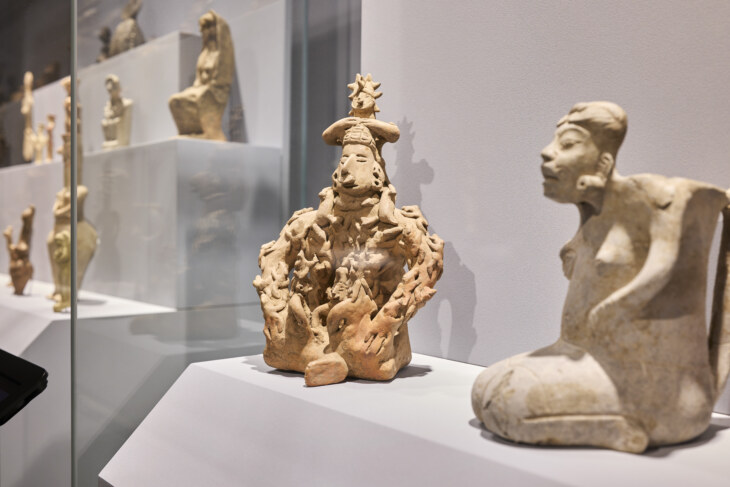 Im Vordergrund zwei Gottheiten-Skulpturen aus Ton der neuen Welt in der archäologischen Sammlung Ebnöther. Im Hintergrund eine Vitrine mit weiteren Ton-Figuren.