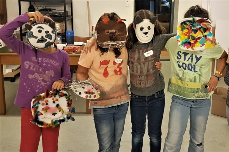 Kinder präsentieren ihre selbstgebastelten Masken vom Erlebnisnachmittag für Klein und Gross.