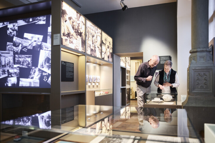 Blick in den Bereich der Industriegeschichte von Schaffhausen. Zwei BesucherInnen stehen vor einem Objekt. Zu sehen sind Fotos von ArbeiterInnen und Objekte der Industriebetriebe.