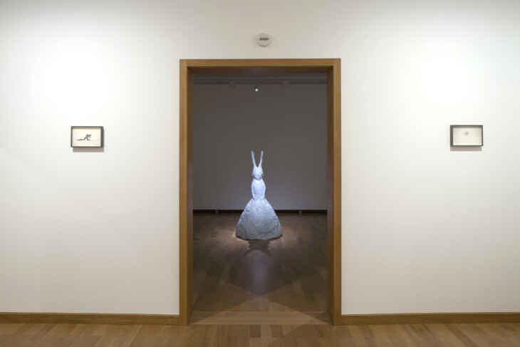 Blick in einen dunklen Raum. Dort steht umrahmt von Türrahmen eine beleuchtete Skulptur von Leiko Ikemura.