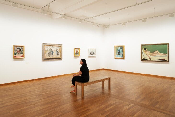 Frau sitzt in der Daueraustellung Kunst. Im Hintergrund sind verschiedene Gemälde von Hodler und Vallonton zu sehen.